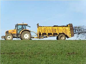 Traktor und Mistzetter beim Ausbringen von Mist auf einem Acker.