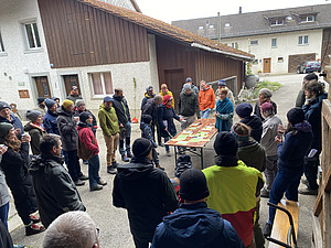 Eine Gruppe steht auf einem Hofgelände um einen Tisch und diskutiert.