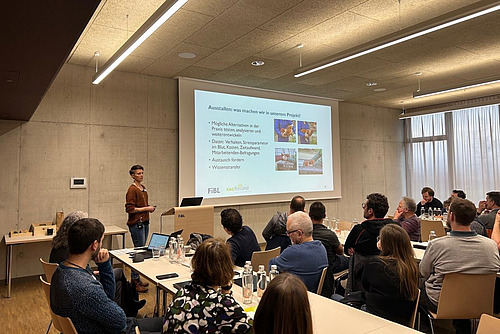 Rednerin präsentiert Teilnehmenden einer Konferenz eine Folie mit dem Titel "Ausstallen: Was machen wir in unserem Projekt".