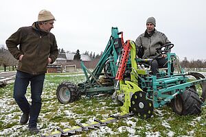 Zwei Männer beschäftigen sich mit einem mannshohen Gerät auf einer Wiese.