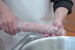 Foto: FiBL, Nele Quander Zwei Hände halten an einer Wurstmaschine eine Salami, die mit Inhalt gefüllt wird.