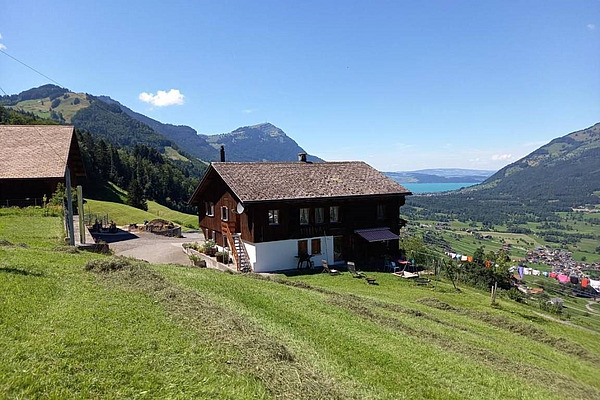 Ein einfaches Wohnhaus am Hang. Im Hintergrund am Horizont ein See.