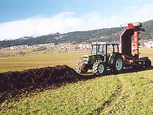 Eine Feldmiete von Mistkompost. Auf der rechten Seite ist ein Traktor mit einer Maschine zusehen, die die Feldmiete kehren wird.